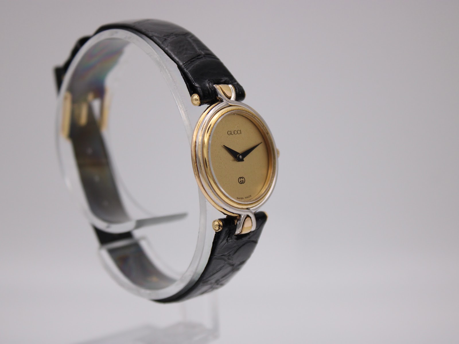 Angled left-side view of the two-tone Gucci 4500 L watch on a clear stand, highlighting the case design.
