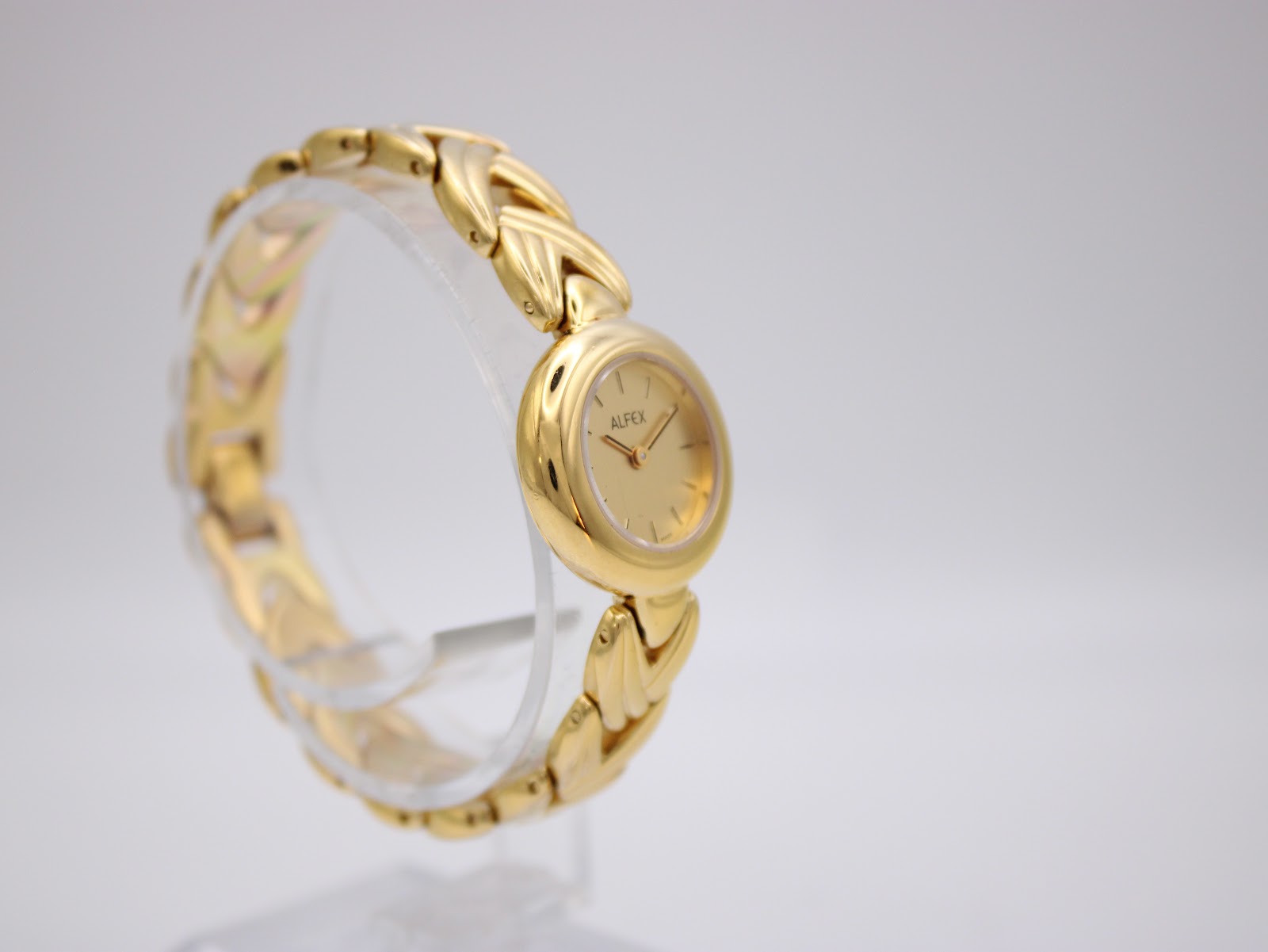 Left side angle view of the Alfex gold watch on a display stand, highlighting the bracelet's texture.