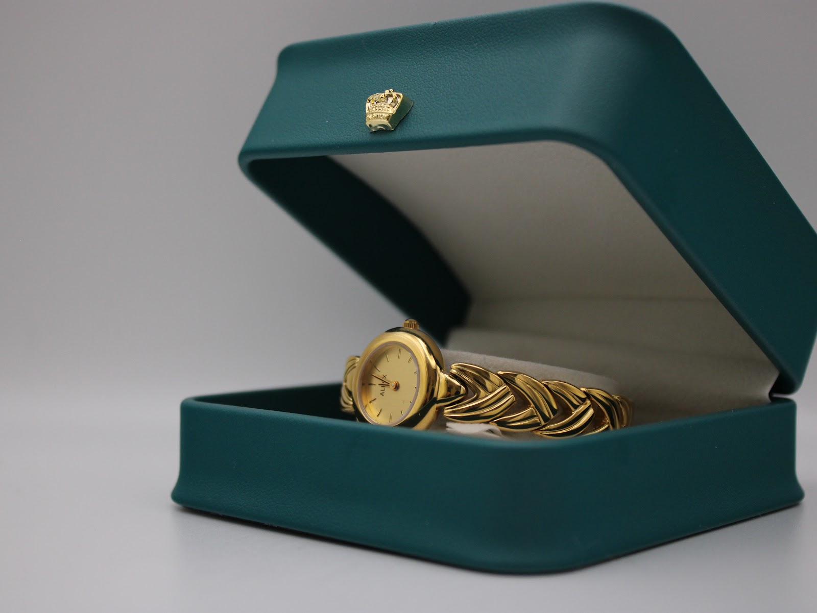 Alfex watch resting inside a teal presentation box with a gold crown emblem.