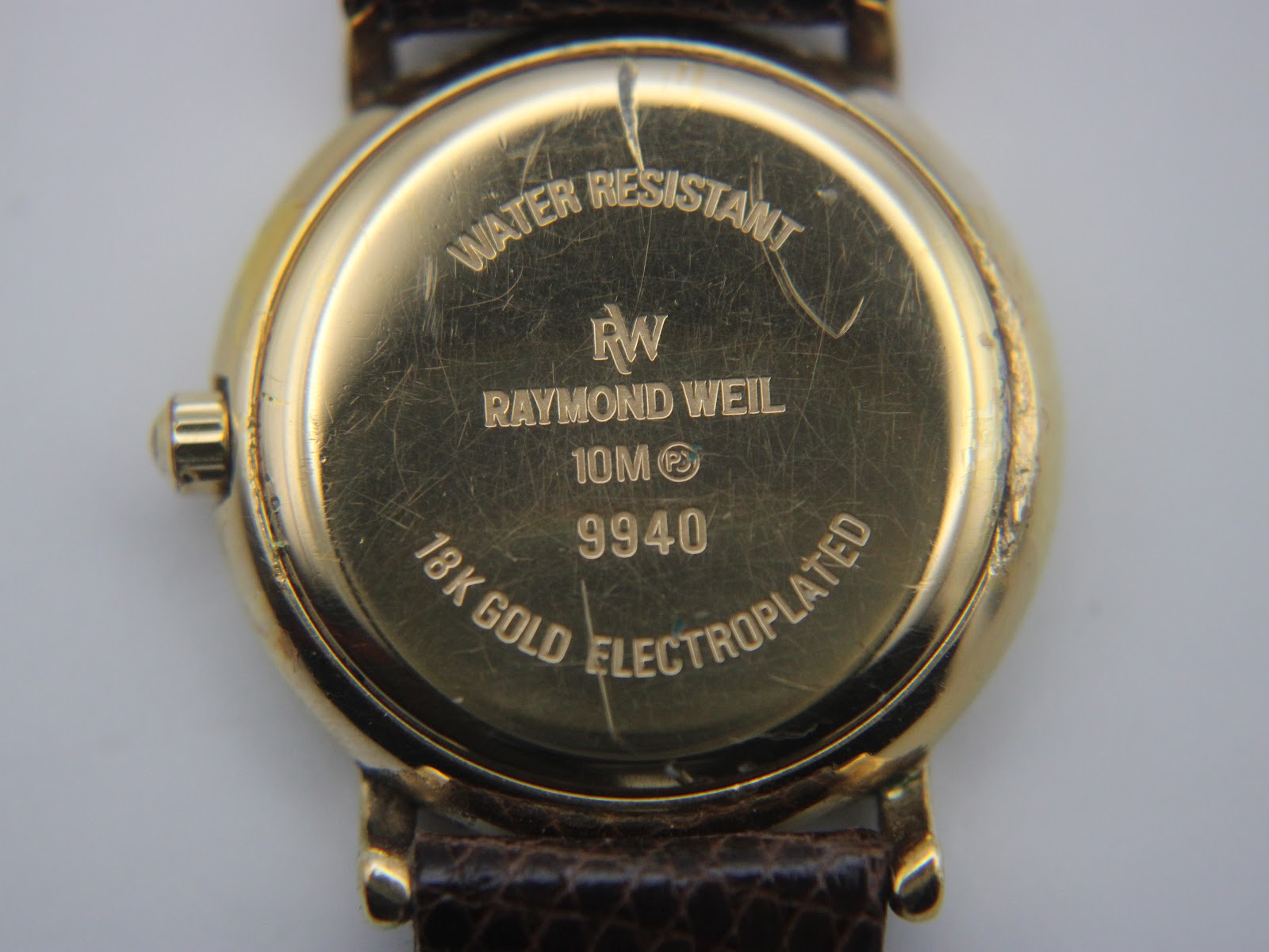 Close-up of the watch case back, engraved with 'WATER RESISTANT', 'RAYMOND WEIL', '9940', '18K GOLD ELECTROPLATED', and a '10M' rating.