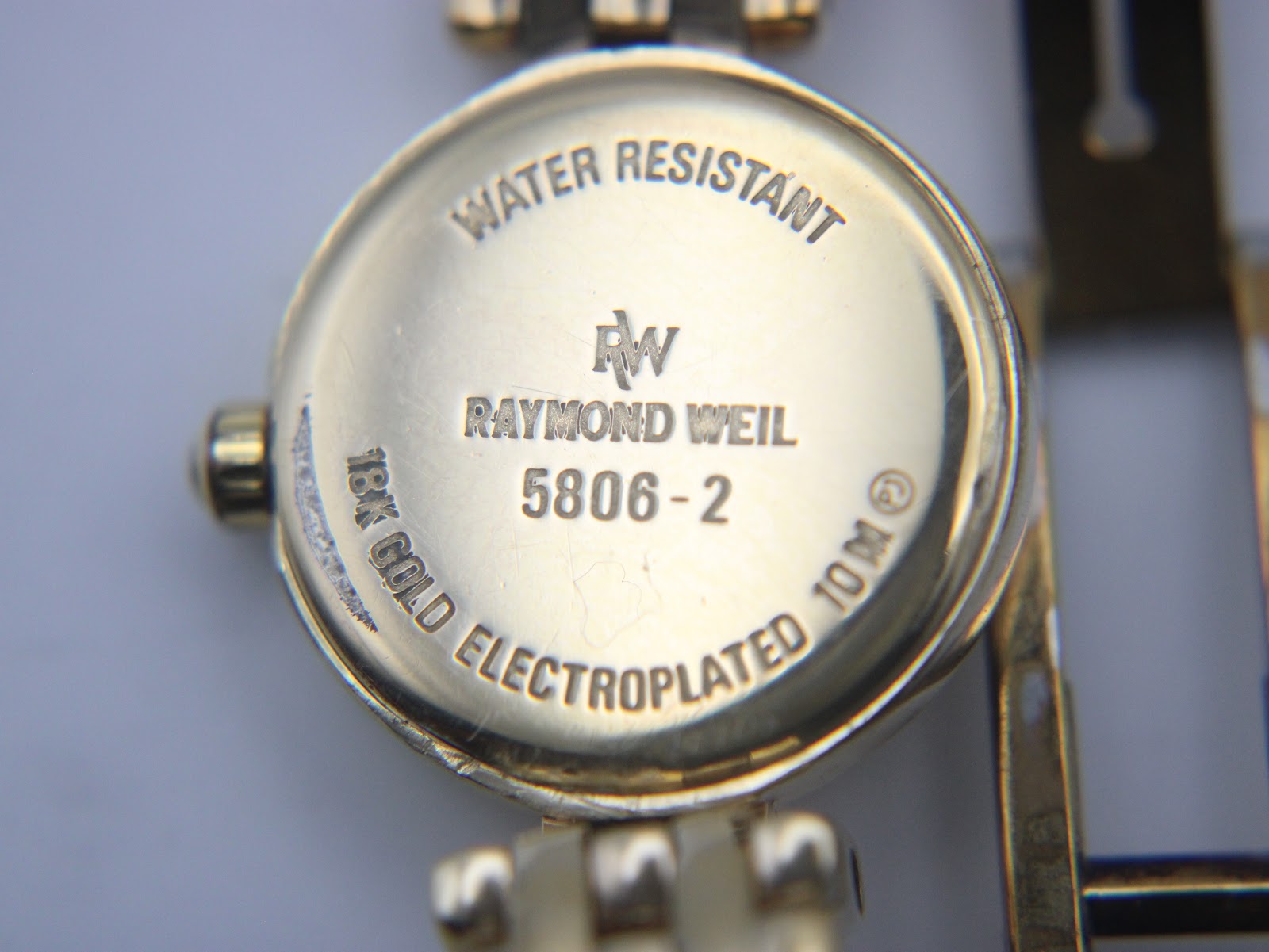 Close-up of the watch's case back, clearly showing "Raymond Weil Geneve 5806-2", "Water Resistant 10 M", and "18K Gold Electroplated".