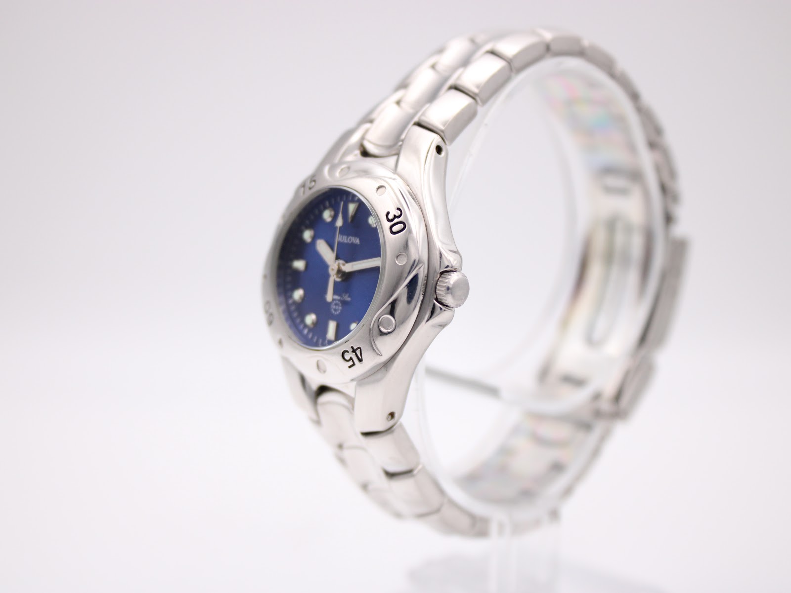 Side profile view of the Bulova Marine Star watch, showing the crown and integrated bracelet design on a clear stand.