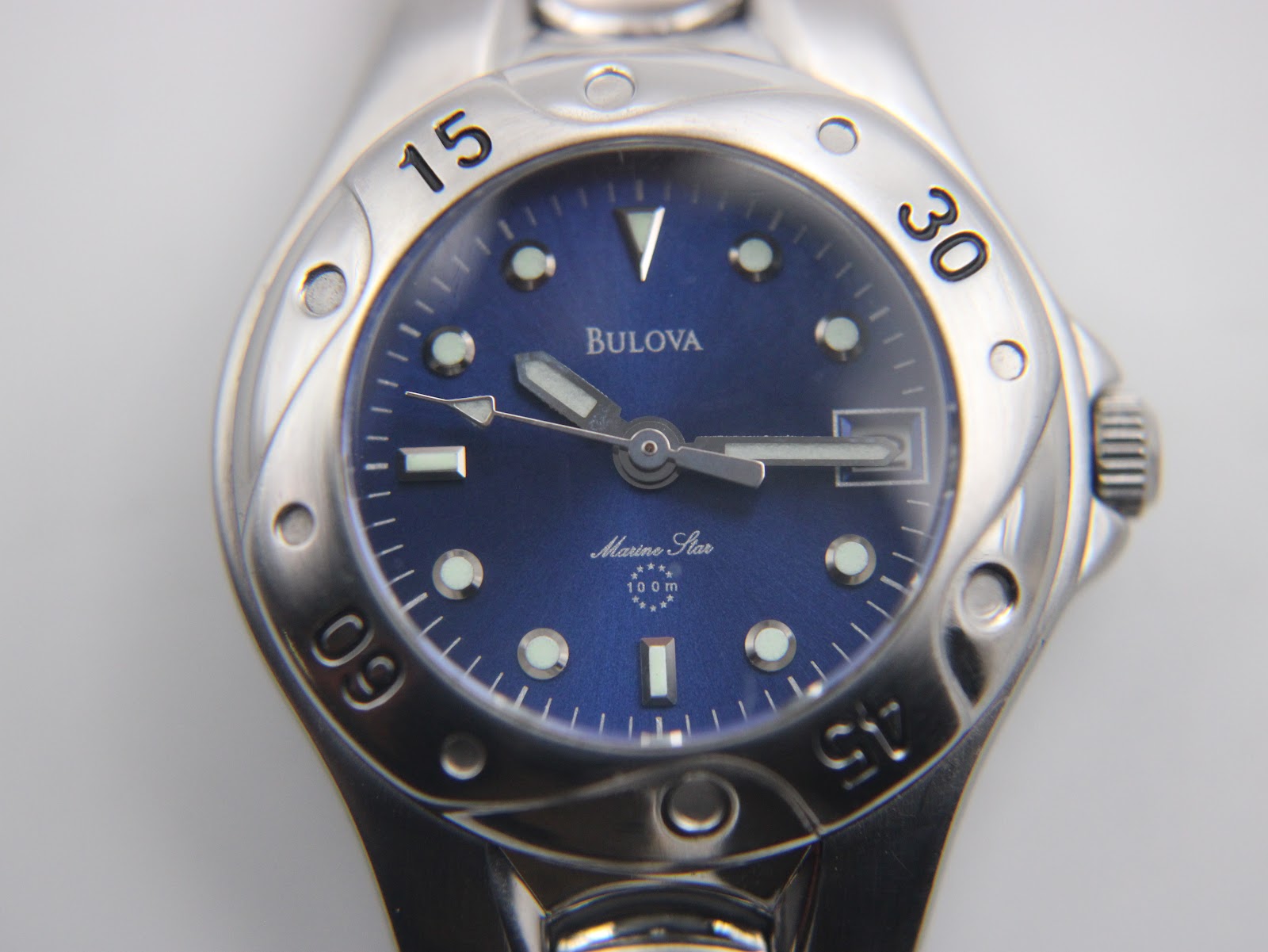 Macro shot of the Bulova Marine Star blue dial, showing luminous dot and baton indices, the date window, "Bulova" and "Marine Star" text, and "100 m" marking.