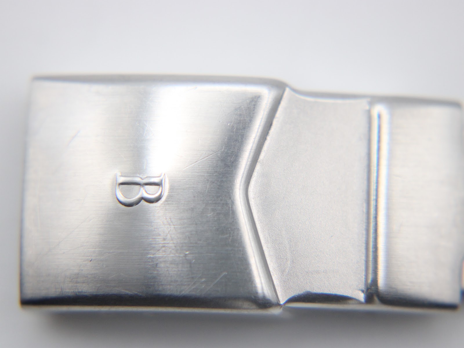 Close-up of the stainless steel bracelet clasp, featuring a raised 'B' logo and a brushed finish.