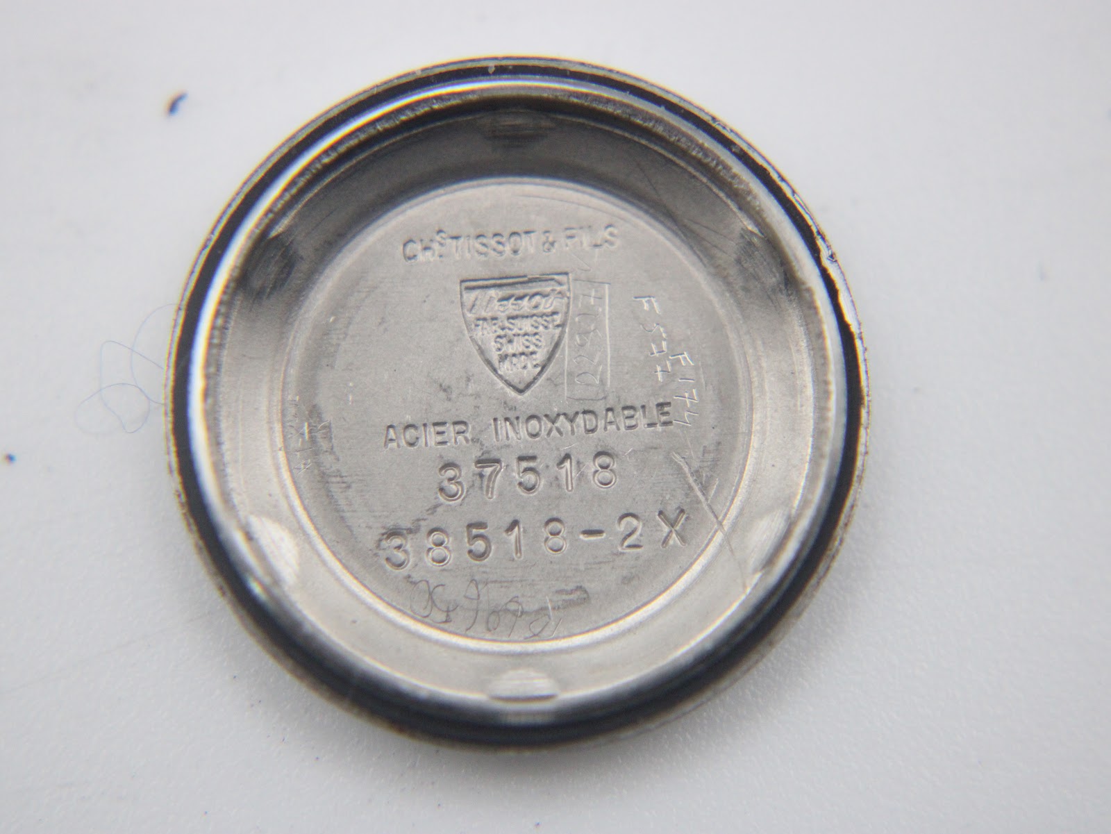 Inside view of the case back, showing 'ACIER INOXYDABLE' (stainless steel), Tissot logo, and serial number '38518-2X'.
