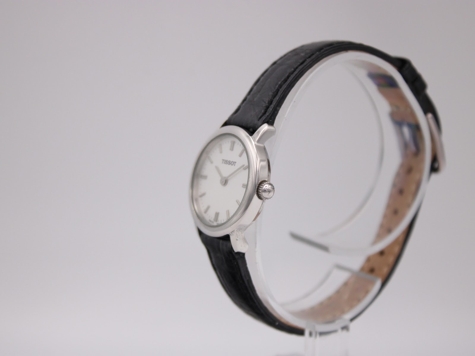 Angled side view of the Tissot C226K watch on a transparent display stand, showing the crown and case profile.