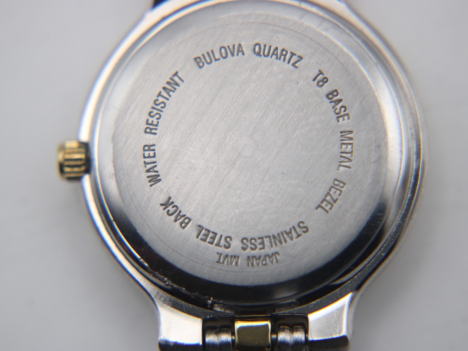 Close-up of the watch case back, engraved with "Bulova Quartz Water Resistant T8 Base Metal Bezel Stainless Steel Back Japan Mvt".
