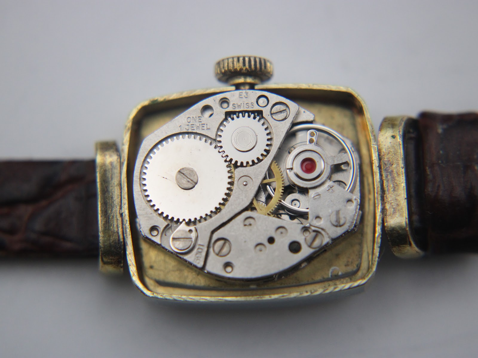 Close-up view of the manual wind Swiss movement, showing gears and 'one jewel' inscription inside the watch case.