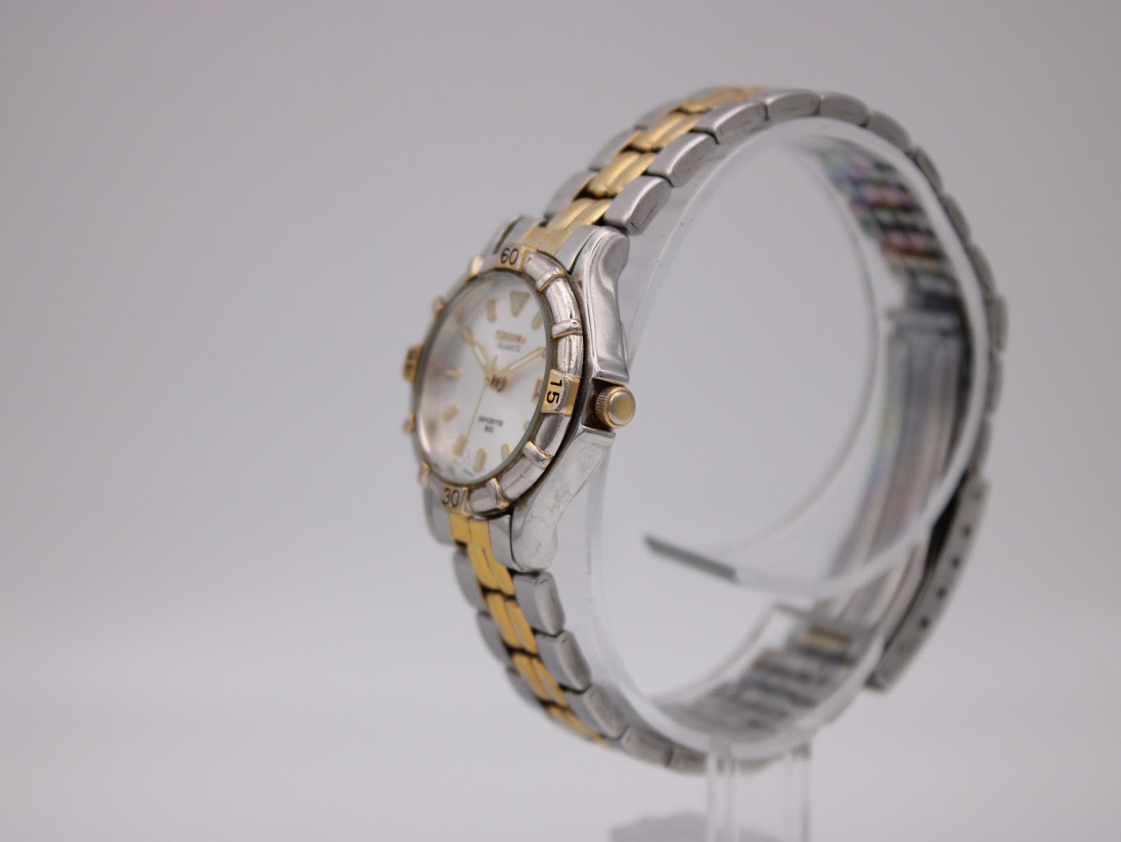 Angled side view of the Seiko watch on a display stand, showing the crown and integrated two-tone bracelet.