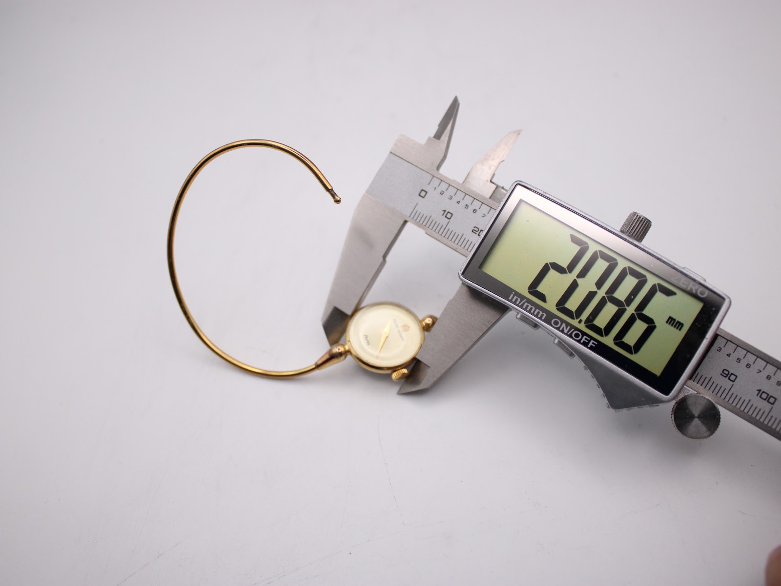 The watch case being measured by a digital caliper, displaying a precise diameter of 20.86mm.