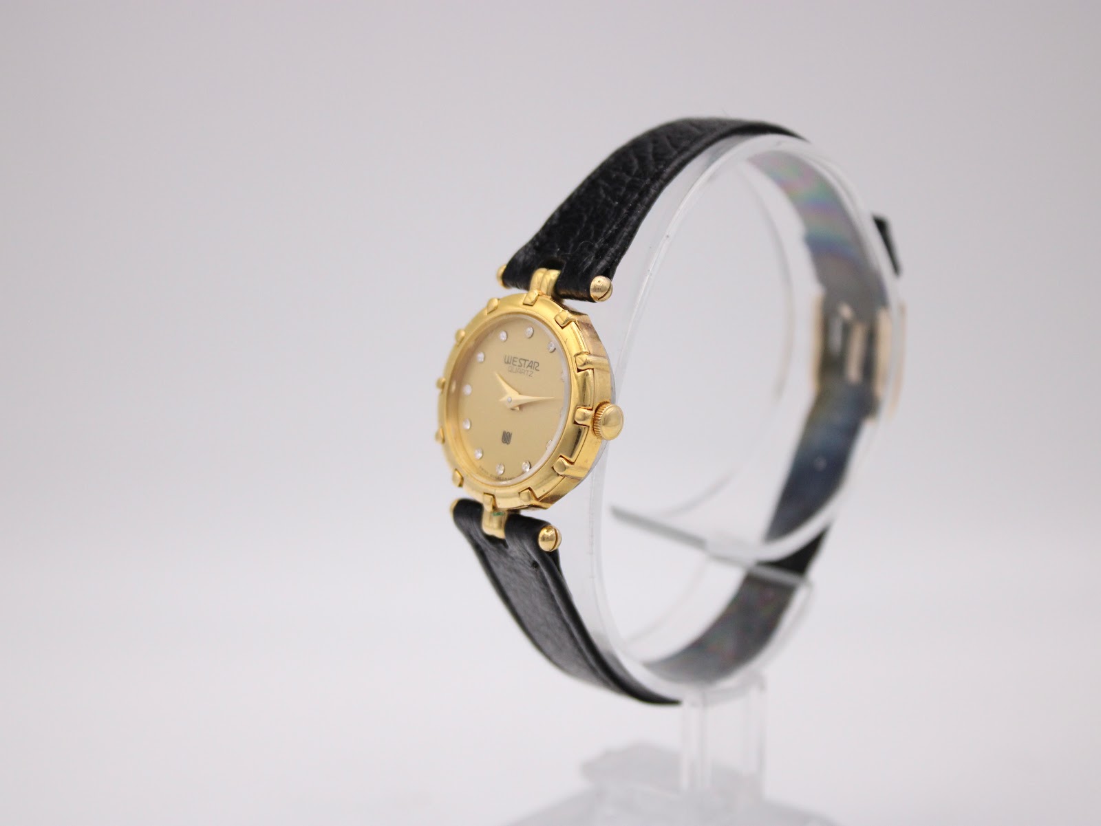 Angled view of the gold Westar watch with champagne dial and black leather strap on a display stand.