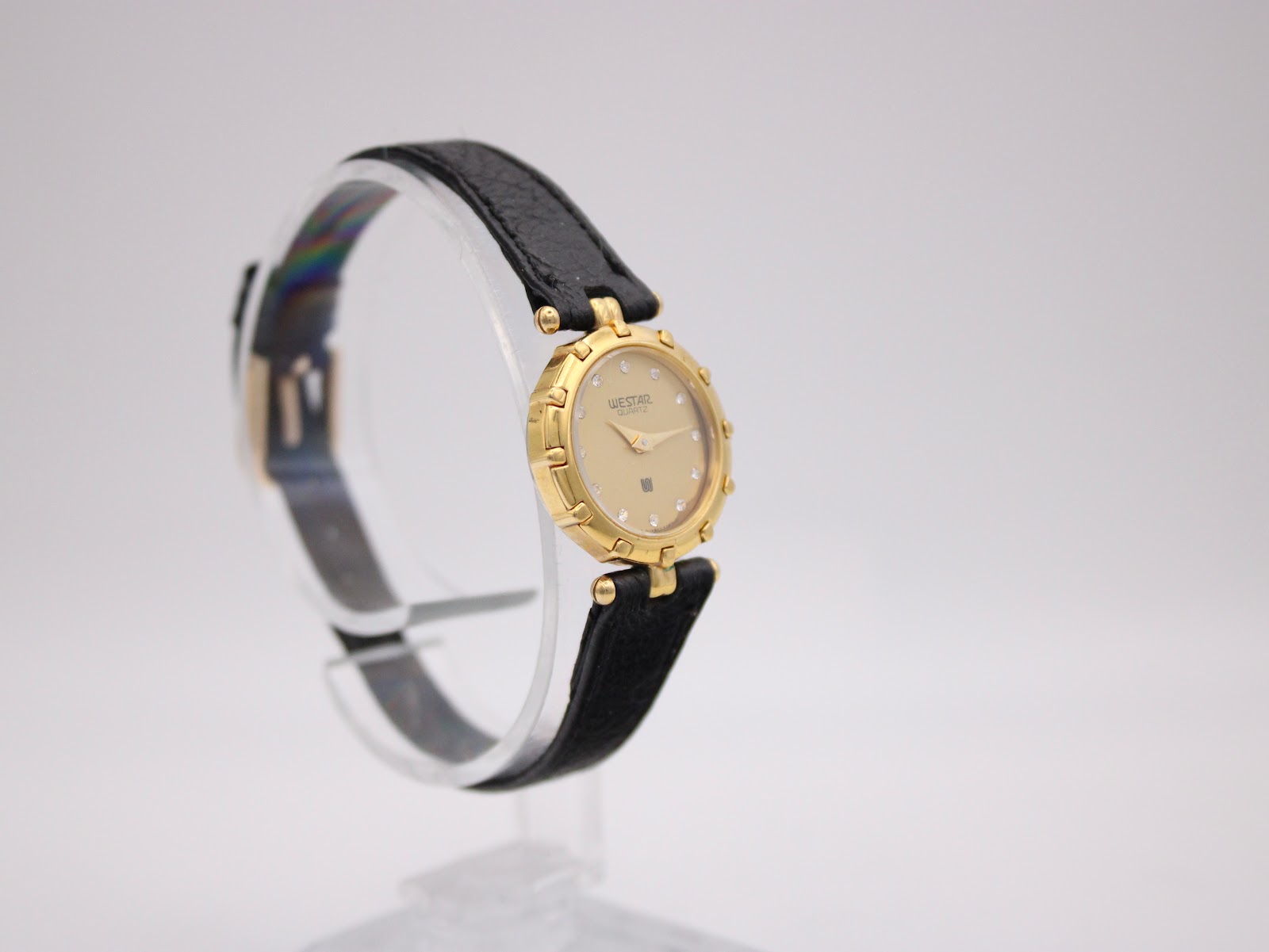 Side view of the Westar gold-toned watch showing the black leather strap and buckle on a display stand.