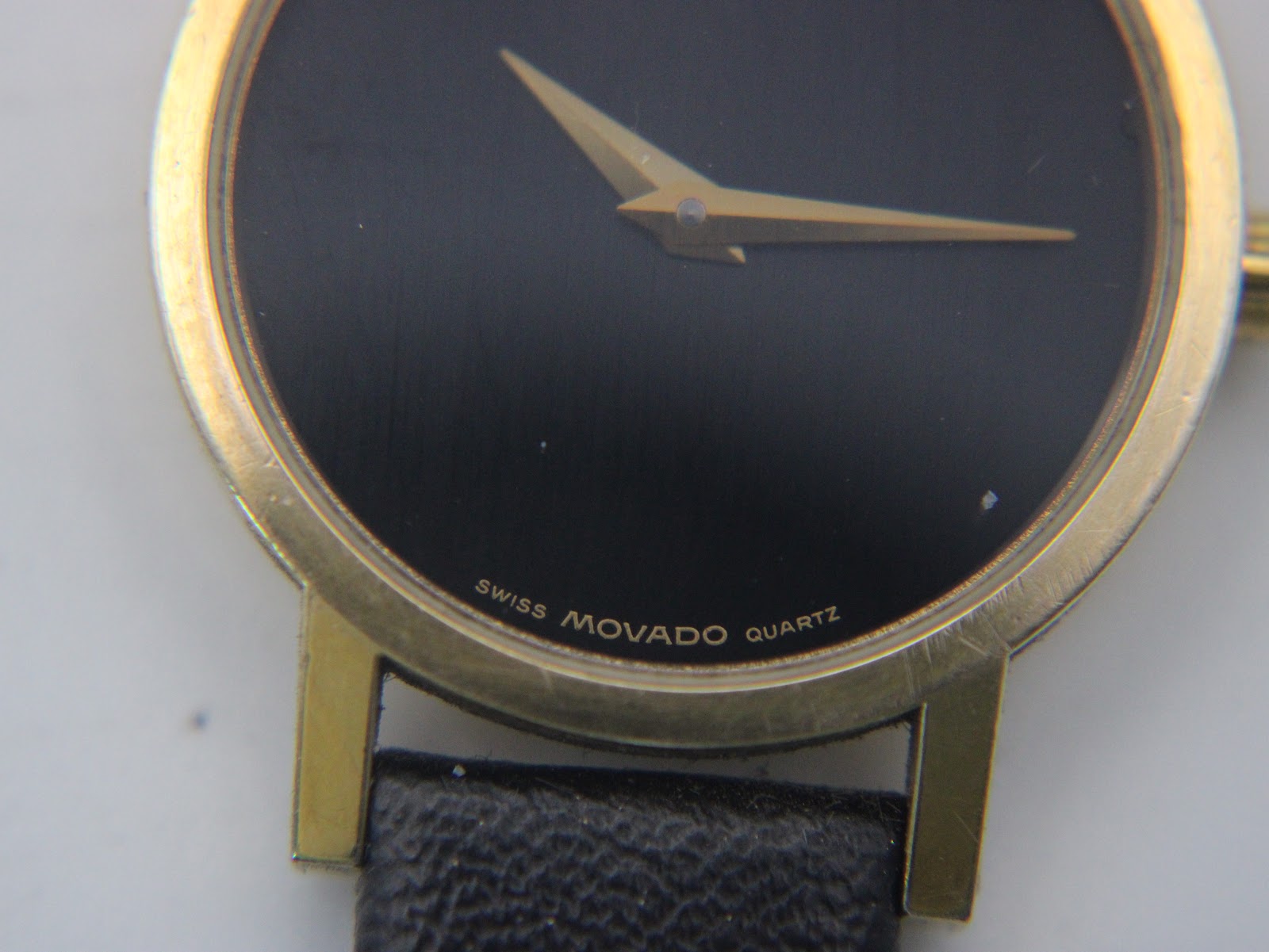 Close-up of the black Movado Museum Dial, showing the iconic gold dot at 12 o'clock, gold hands, and "Swiss Movado Quartz" text.