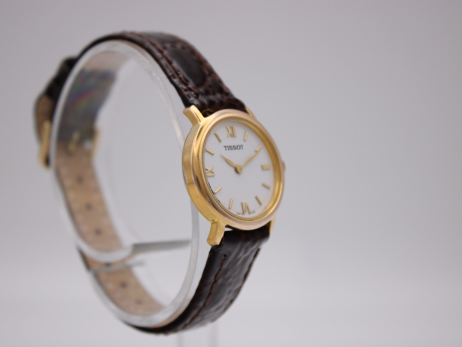Another angled side view of the Tissot C225K watch on a stand, showing the brown leather strap and gold-tone buckle.