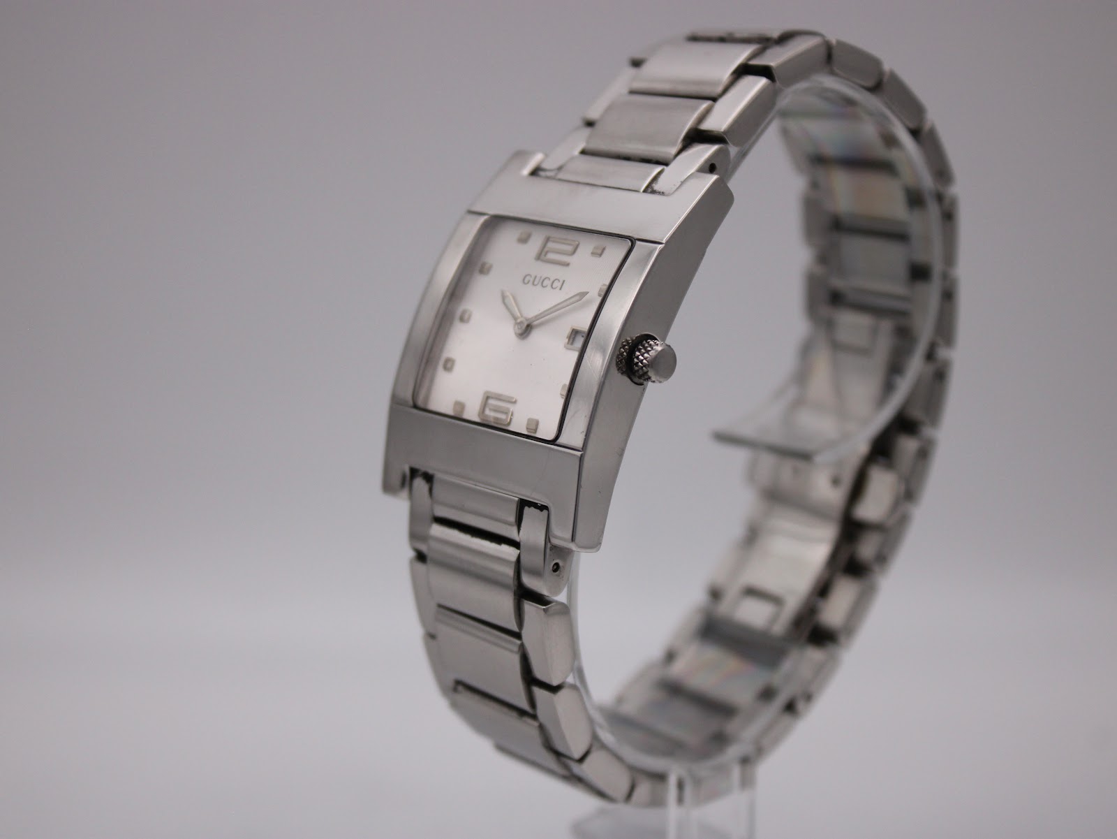 Angled side view of the Gucci 7700 M watch on a display stand, showcasing its polished crown and the curved profile of the integrated steel bracelet.
