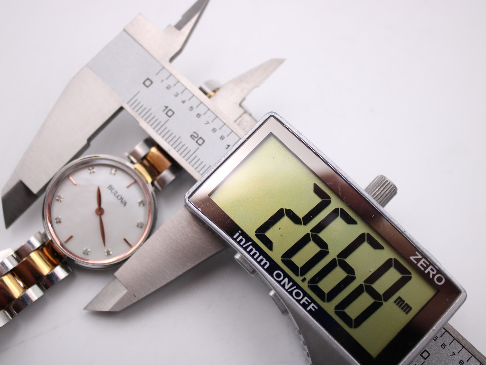 Top-down view of the watch case being measured by a digital caliper, showing 26.66 mm diameter.