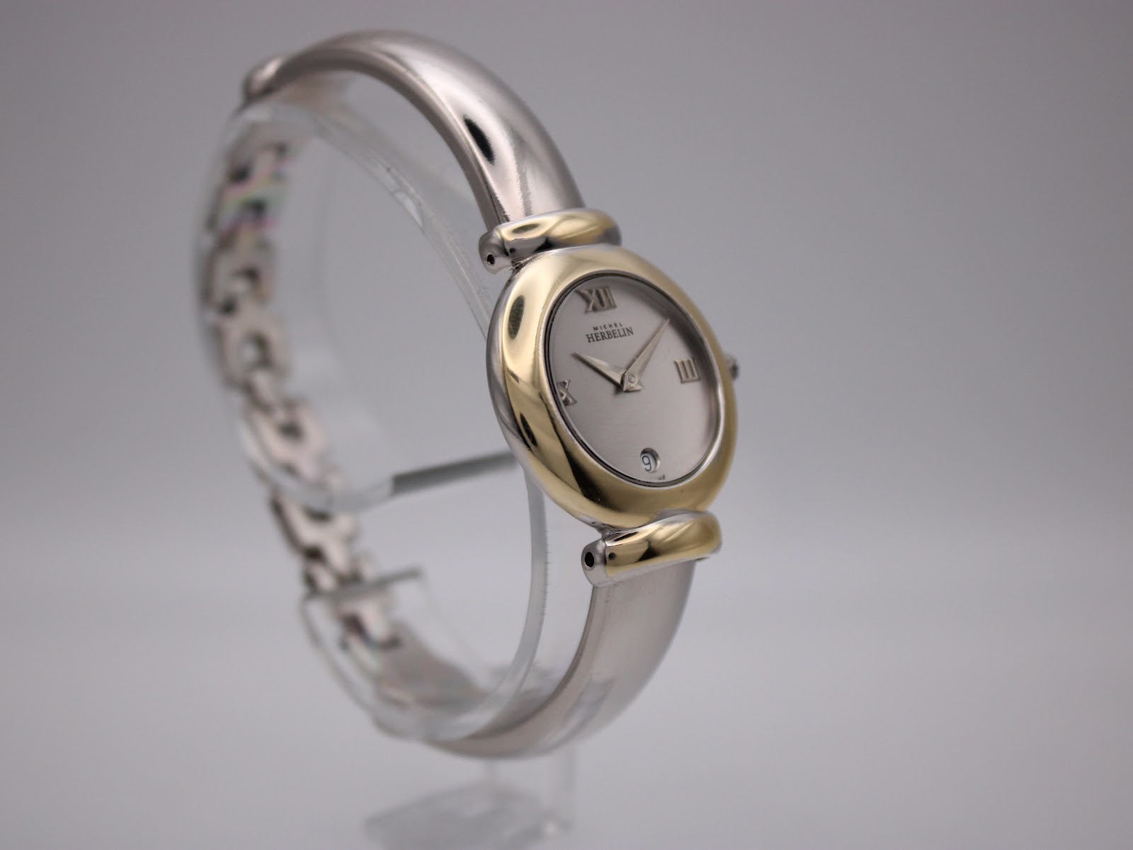 Side-angled view of the Michel Herbelin watch on a stand, highlighting the integrated two-tone bangle and gold-tone bezel.