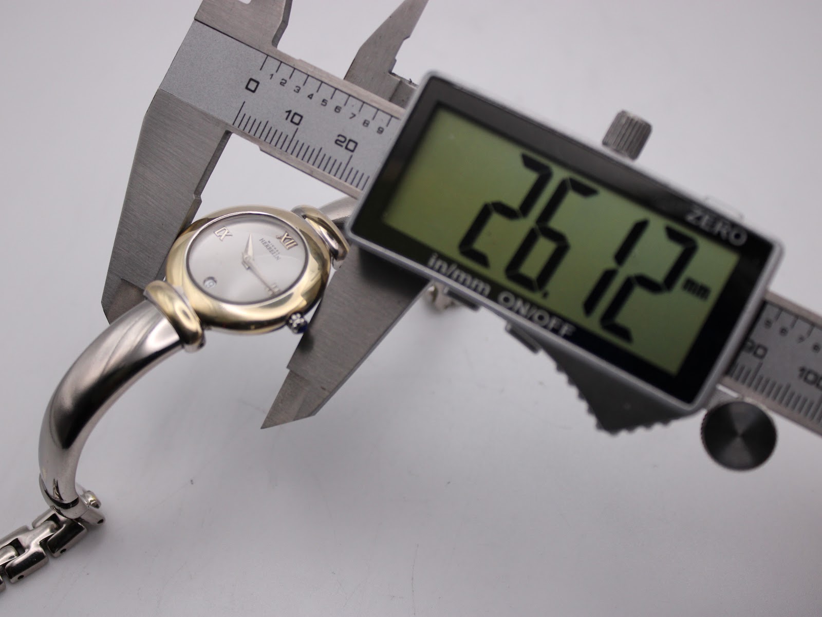 Digital caliper measuring the watch case diameter at 26.12mm, with the watch visible.