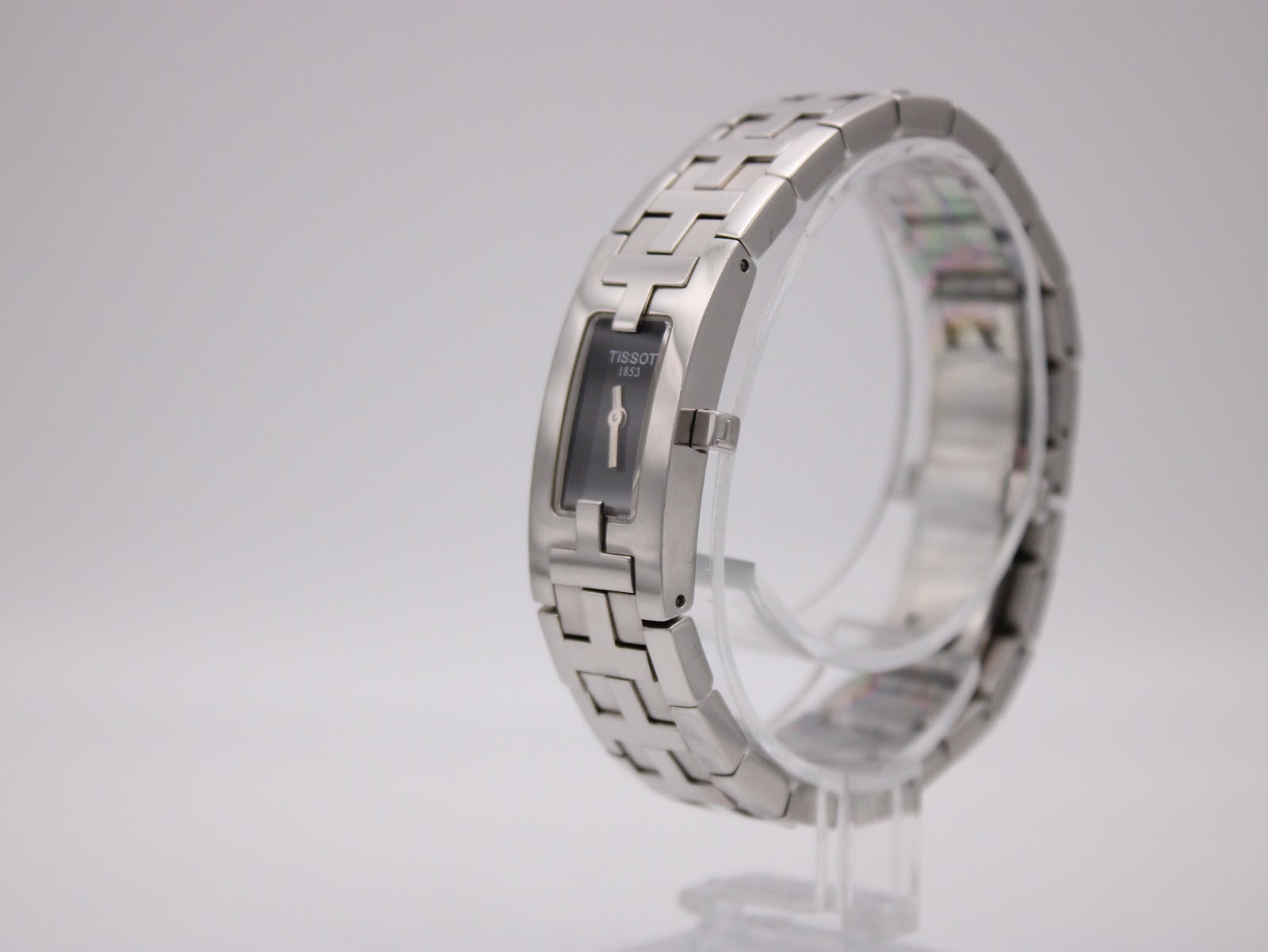 Angled side view of the Tissot L820P watch on a clear stand, showing the curved profile of the integrated bracelet.