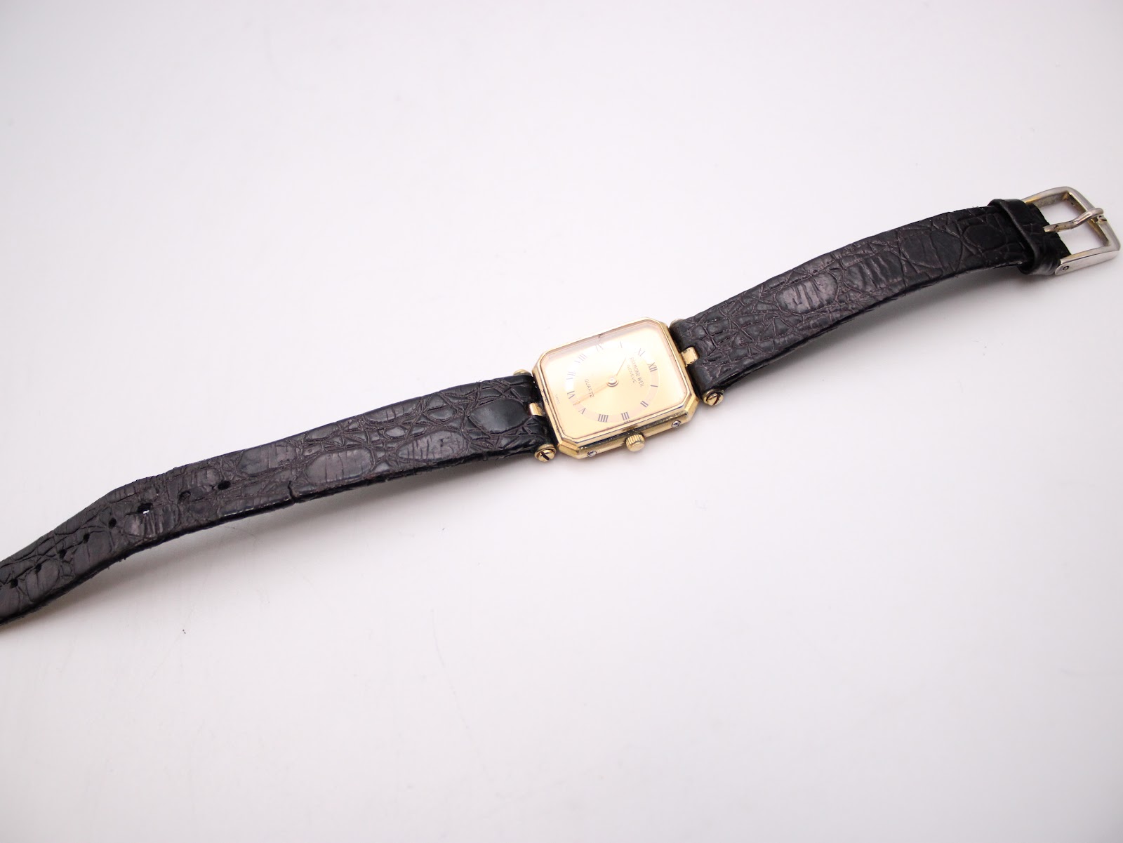 Overhead view of the Raymond Weil watch with its black textured leather strap fully extended, showing the gold-tone buckle.