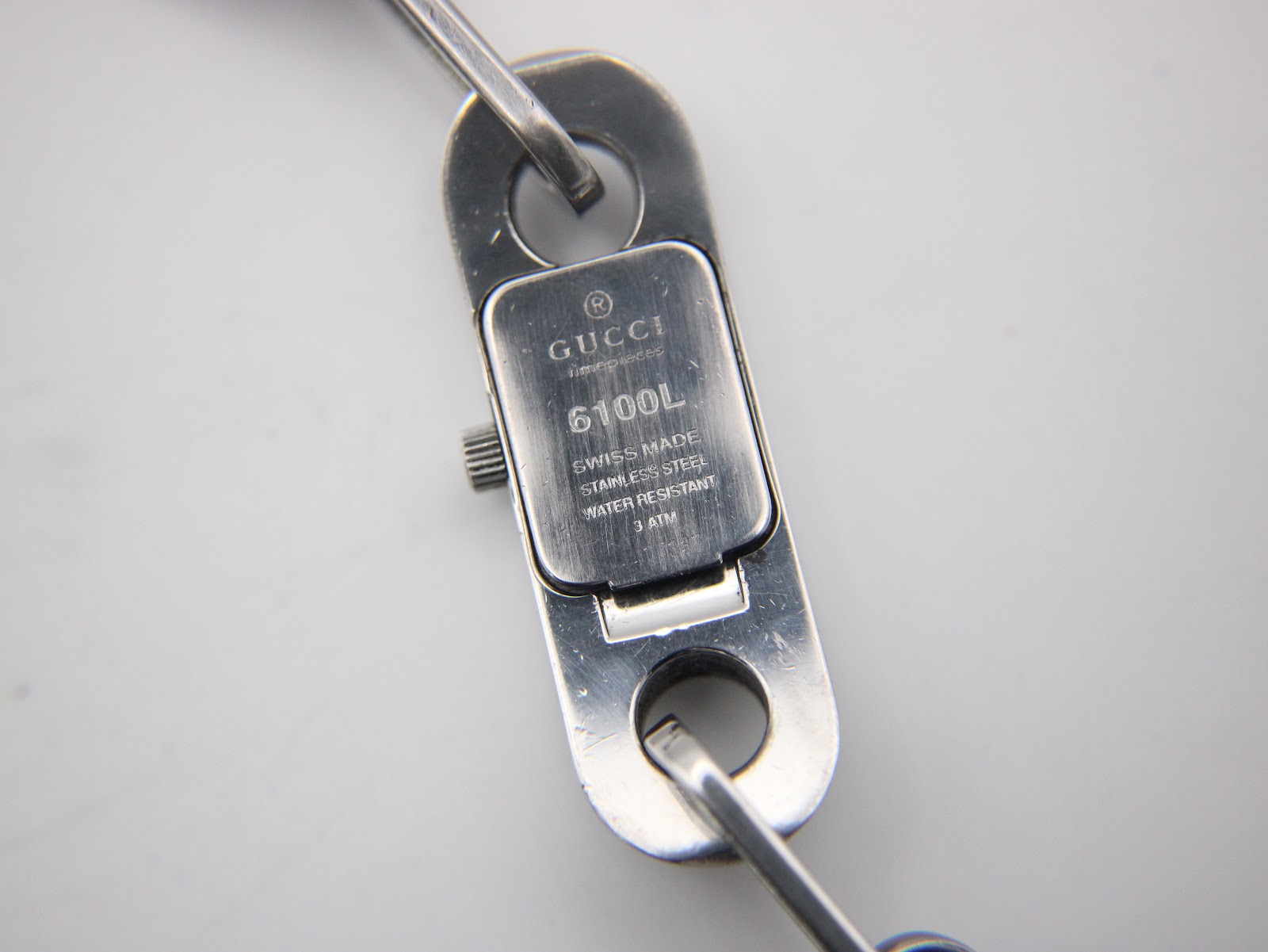 Close-up of the watch case back, showing engravings: "GUCCI", "6100L", "SWISS MADE", "STAINLESS STEEL", "WATER RESISTANT", "3 ATM".