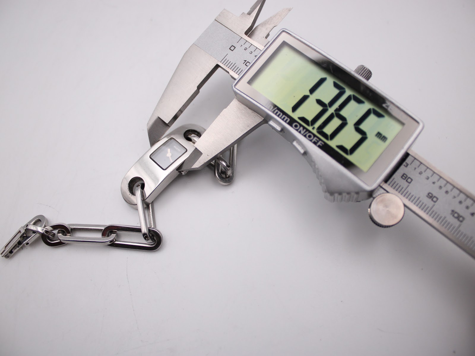 Digital caliper measuring the width of the watch case, displaying a precise measurement of 13.65 mm.