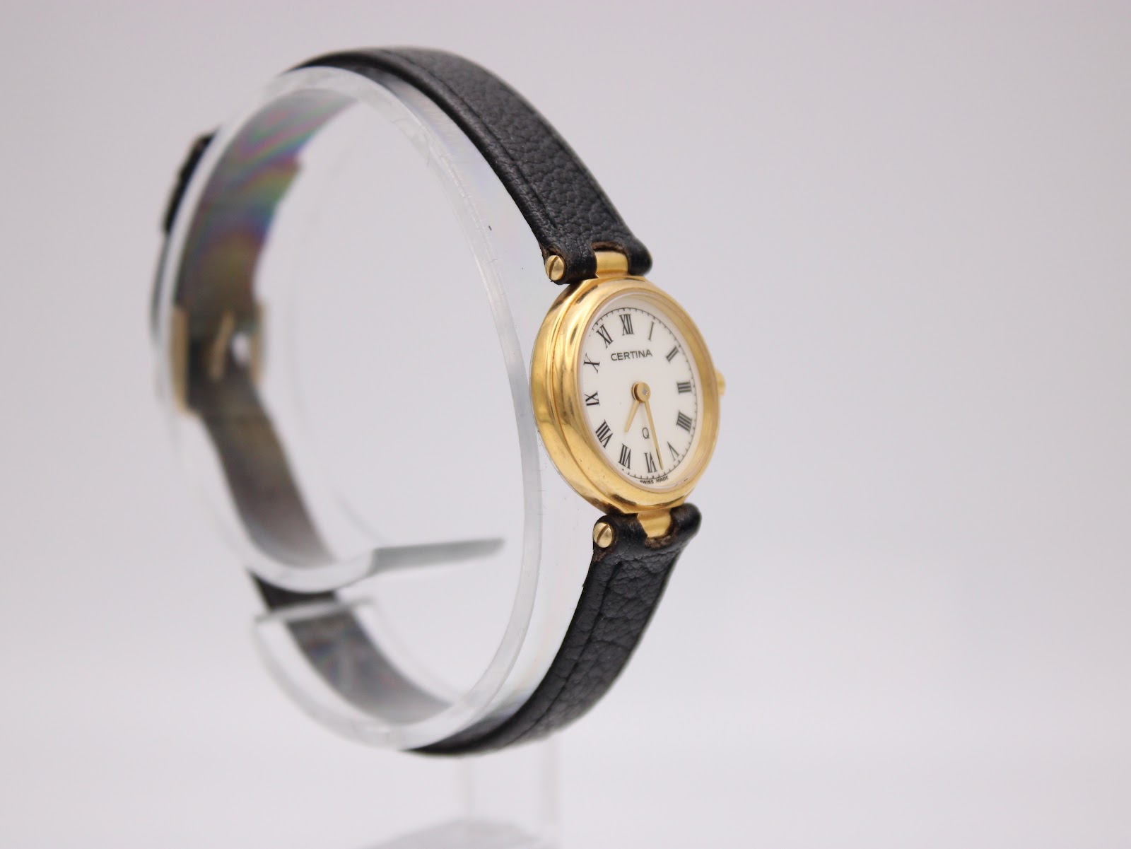 Angled right view of Certina ladies' watch on stand, showing gold case and black leather strap.