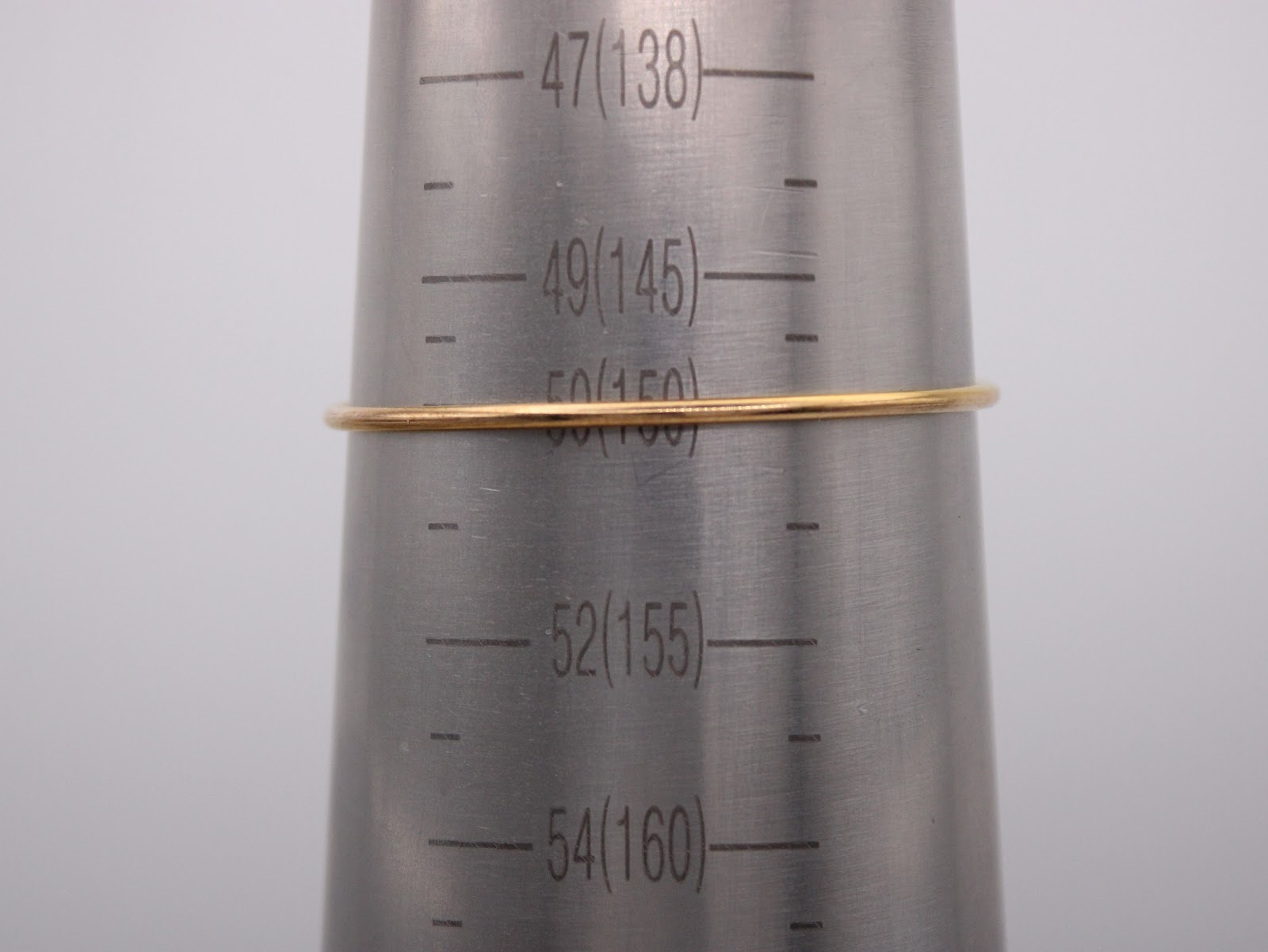 The gold bangle bracelet positioned on a metal wrist sizing cone, indicating a size of approximately 150mm circumference.