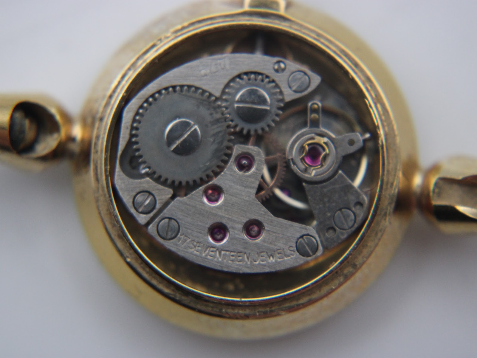 Macro view inside the watch, showing the exposed manual wind mechanical movement with visible gears and '17 seventeen jewels' inscription.