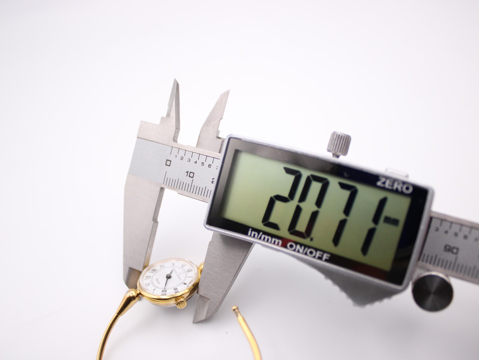 A digital caliper precisely measuring the watch case diameter at 20.71mm, with the watch resting on a white surface.