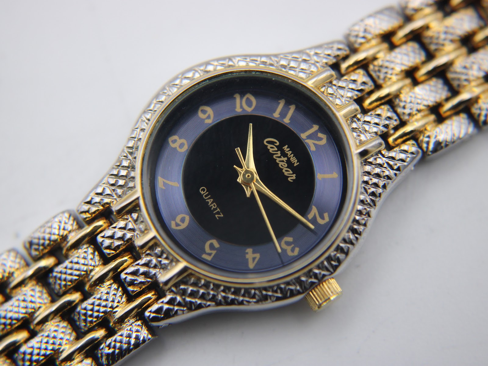 Close-up of the Manin Cartear black dial, gold Arabic numerals, and textured two-tone bracelet.