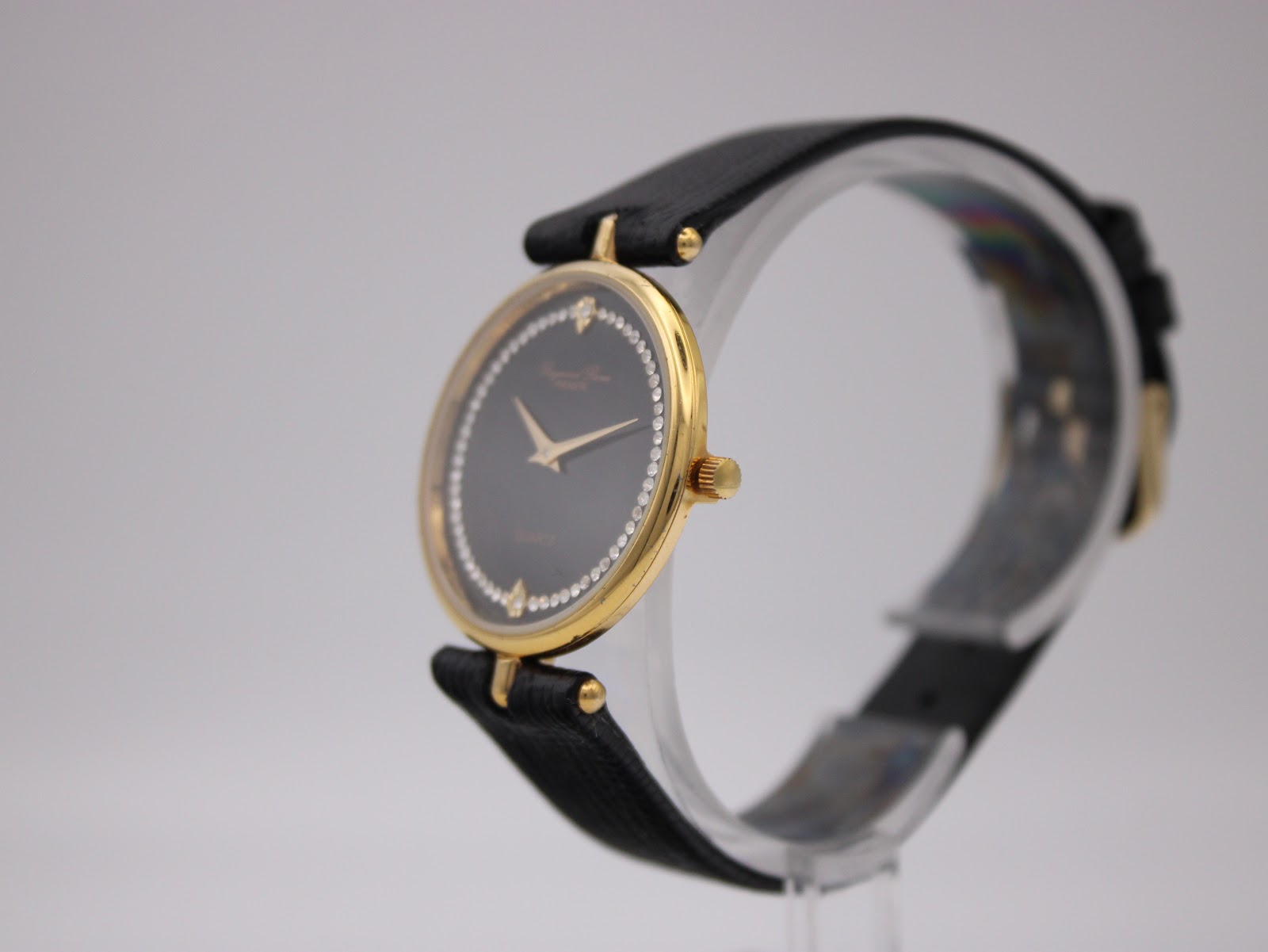 Angled side view of the Raymond Rone watch on a clear stand, highlighting its slim profile and gold-plated case.