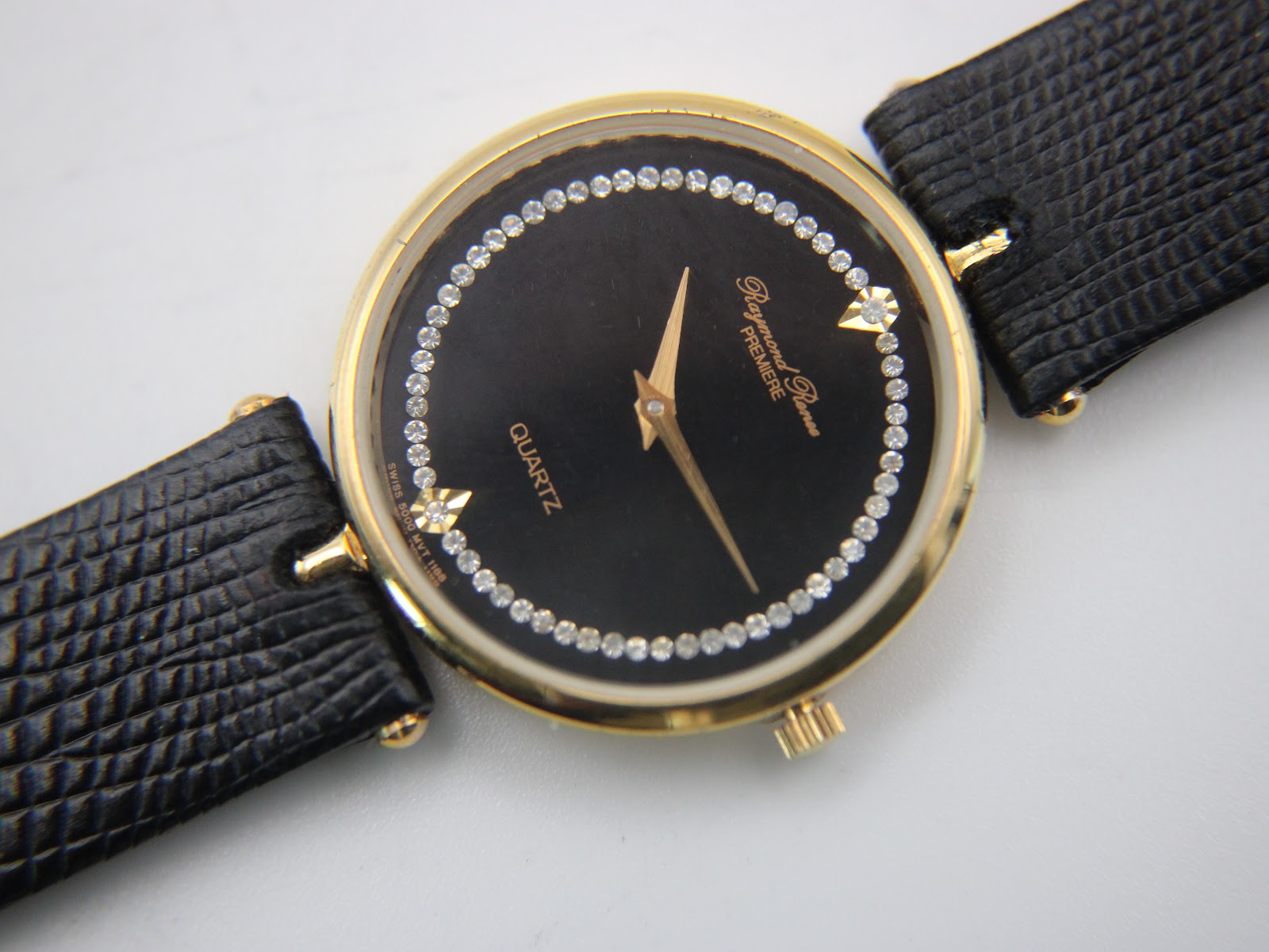 Detailed close-up of the black dial with gold hands, diamante hour markers, and brand/model text.