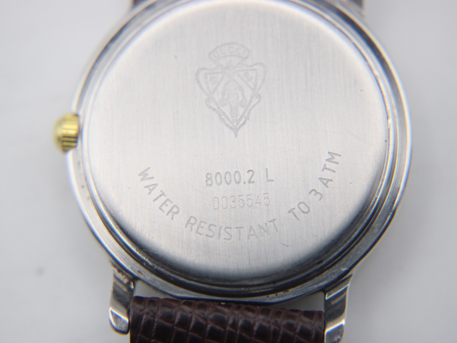 Close-up of the watch case back, showing the Gucci logo, model 8000.2 L, serial number 0035545, and 'water resistant to 3atm' engraving.