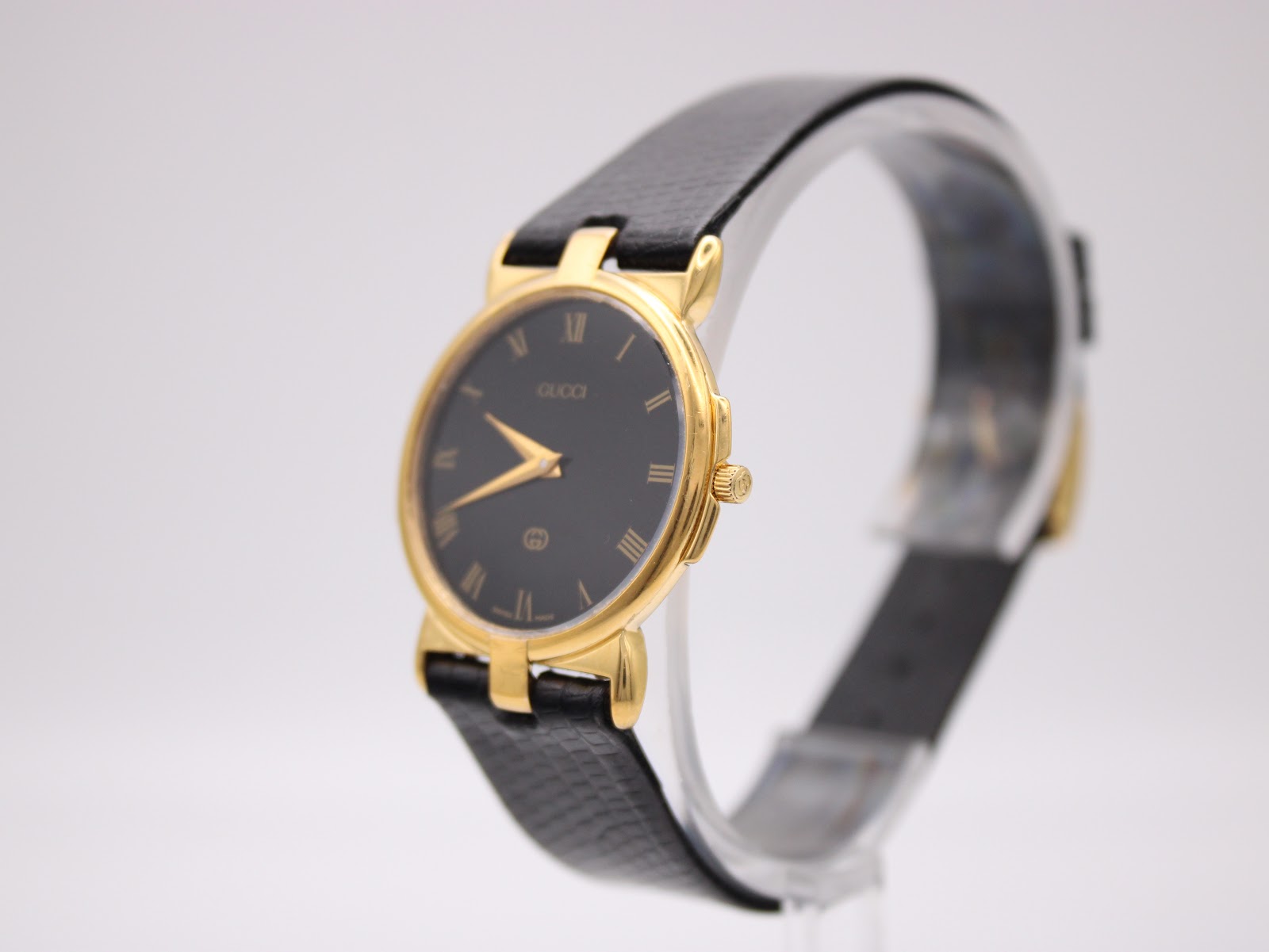 Angled side view of the Gucci 3400M watch on a clear display stand, showing the crown and case profile.
