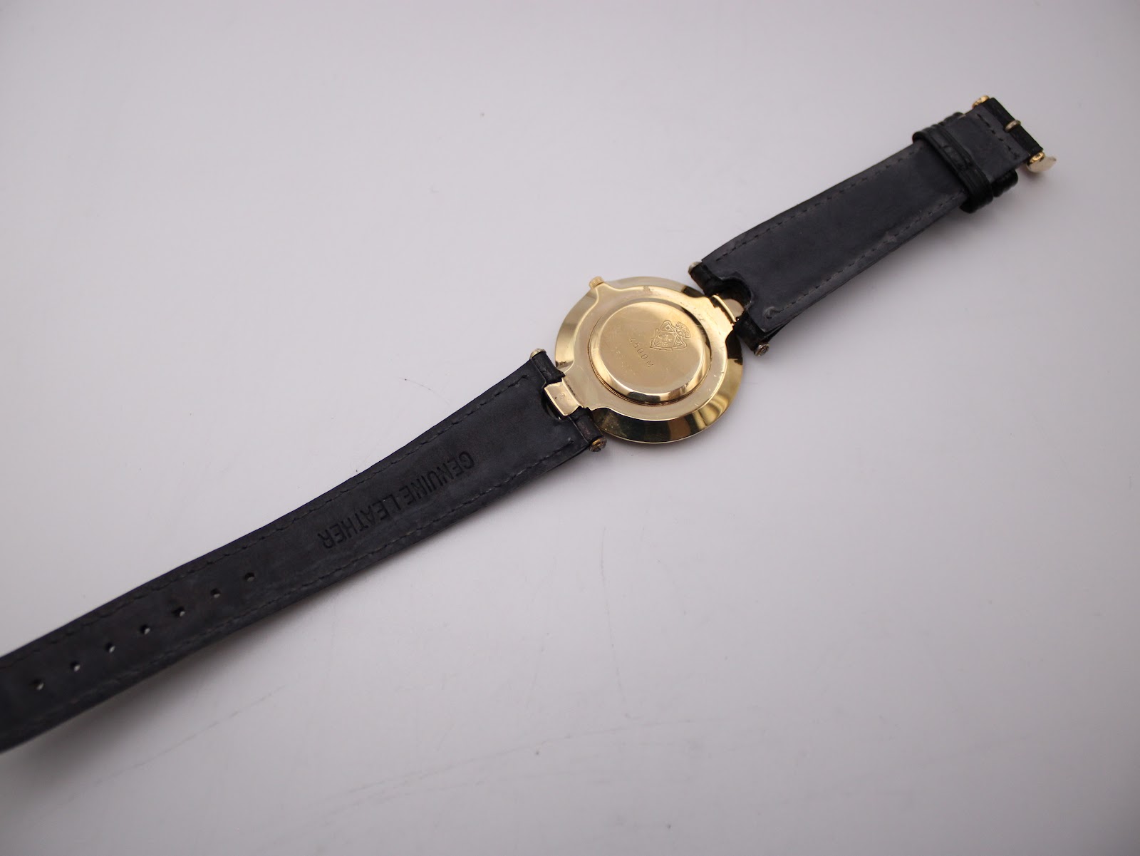 Back view of the entire Gucci 4500 M watch, showing the gold-tone case back and the 'GENUINE LEATHER' marking on the strap lining.