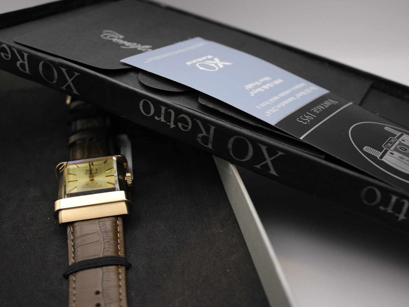 The XO RETRO watch resting in its original black presentation box, with accompanying papers visible.