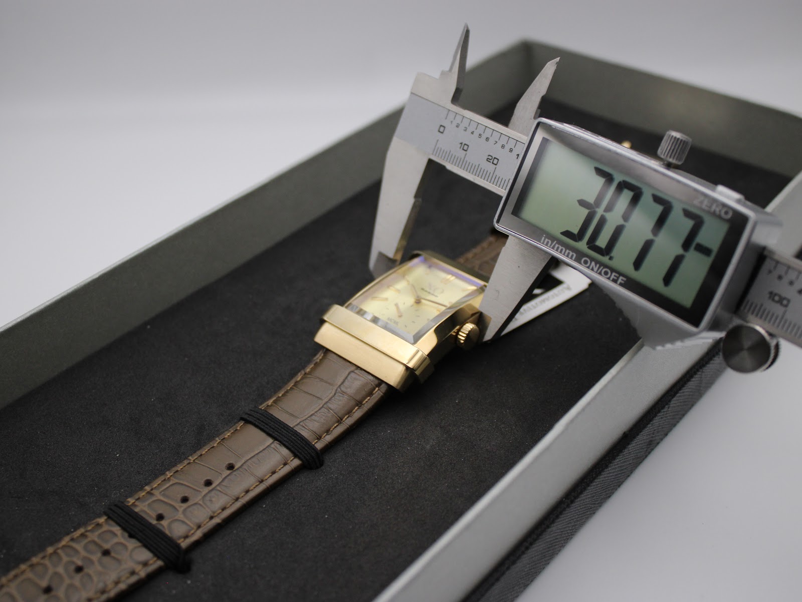 Digital caliper measuring the width of the XO RETRO watch case at 30.77mm, showing the watch inside its box.