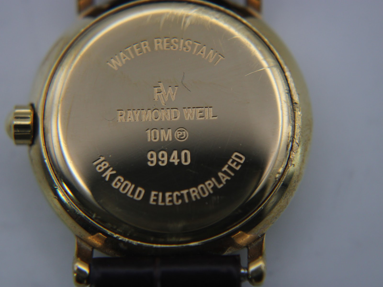 Close-up of the gold electroplated case back, showing 'water resistant 10M', 'Raymond Weil', '9940', and '18k gold electroplated' engravings with minor scratches.