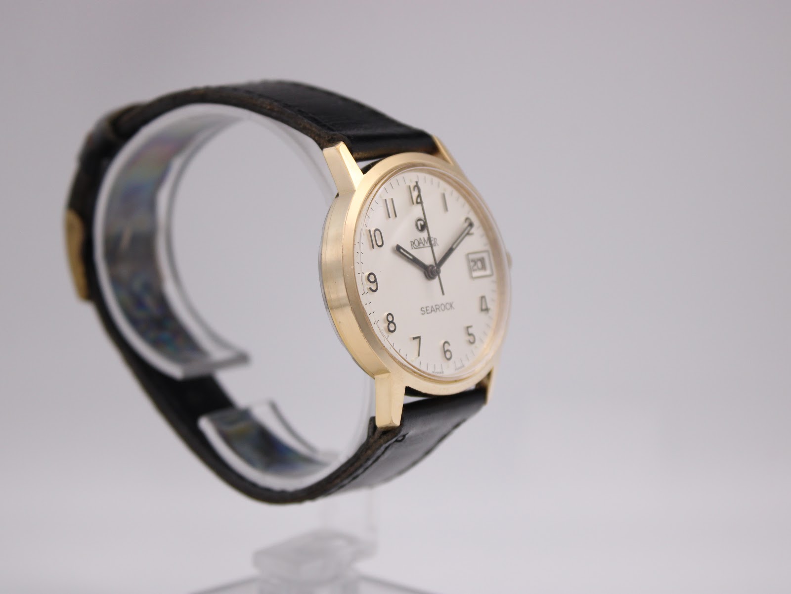 Left-side angled view of the Roamer Searock watch, highlighting the gold tone case profile and black leather strap.