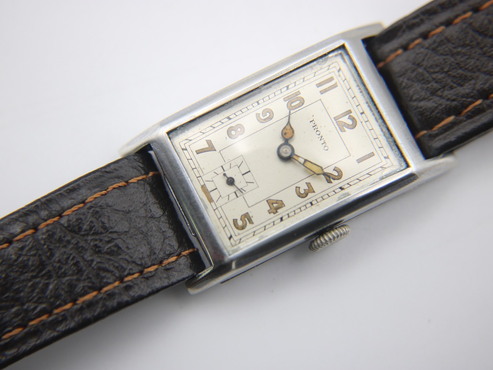 Angled close-up of the PRONTO watch dial, showcasing the cream face, legible Arabic numerals, and small seconds sub-dial.