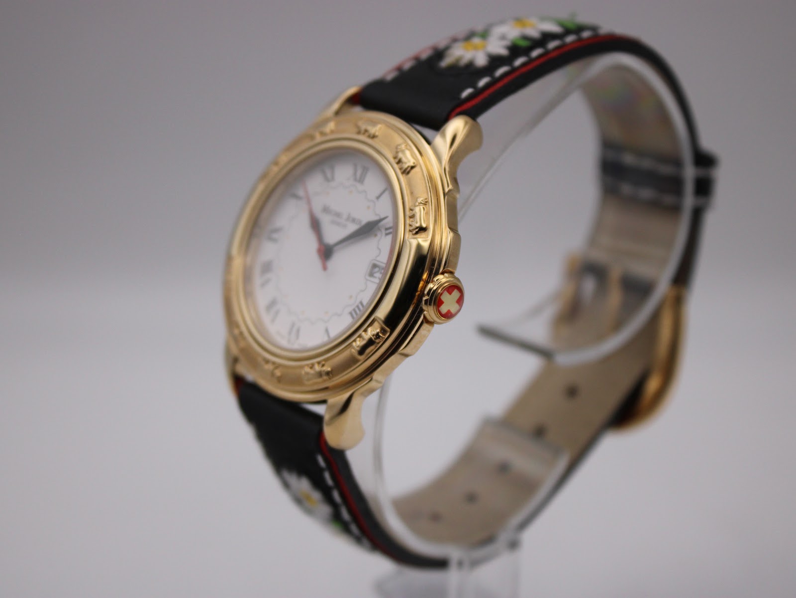 Angled side view of the watch on a display stand, highlighting the profile of the gold tone case and the red Swiss cross crown.