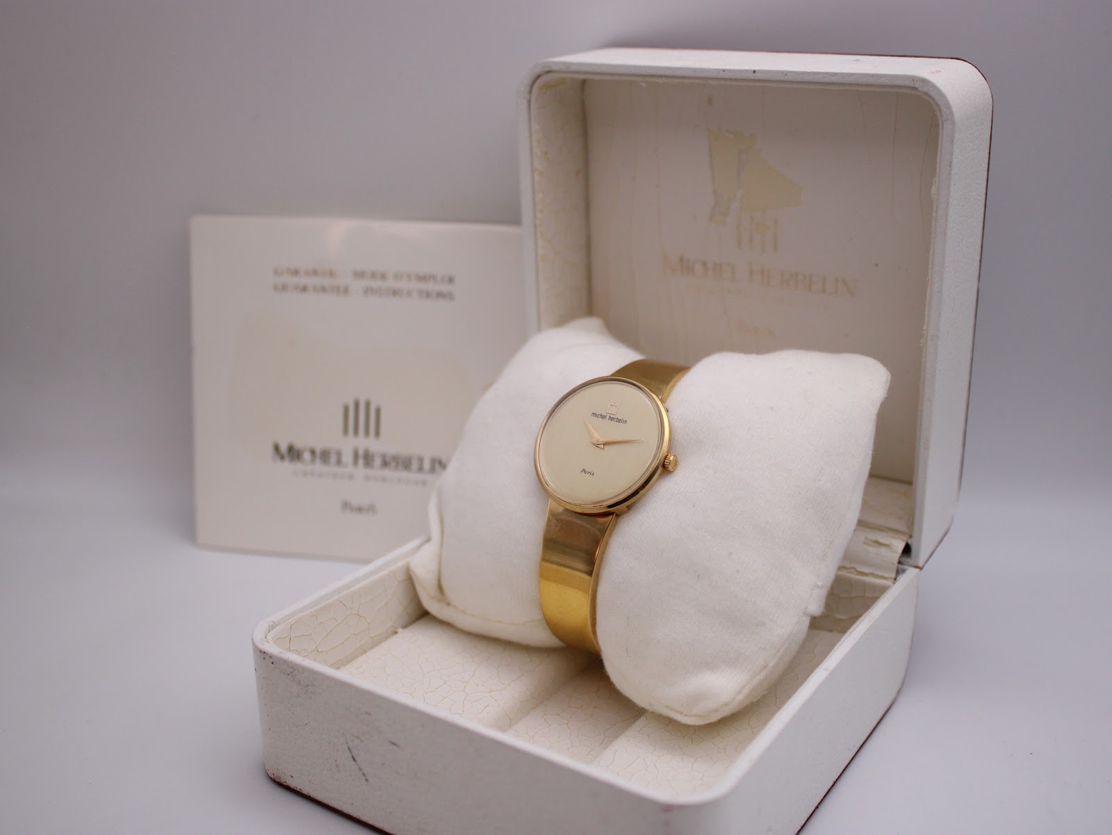 The Michel Herbelin watch resting in its original white box, with accompanying papers visible in the background.