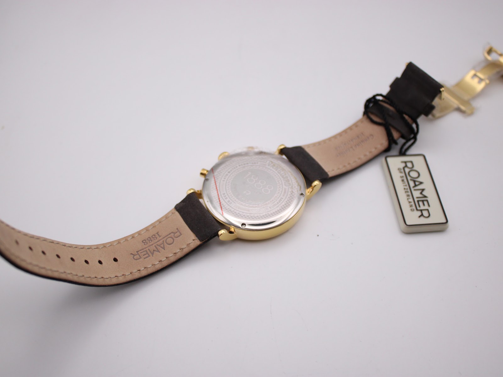 Back view of the watch and strap laid flat, showing the case back with protective film and the interior of the leather strap with branding.