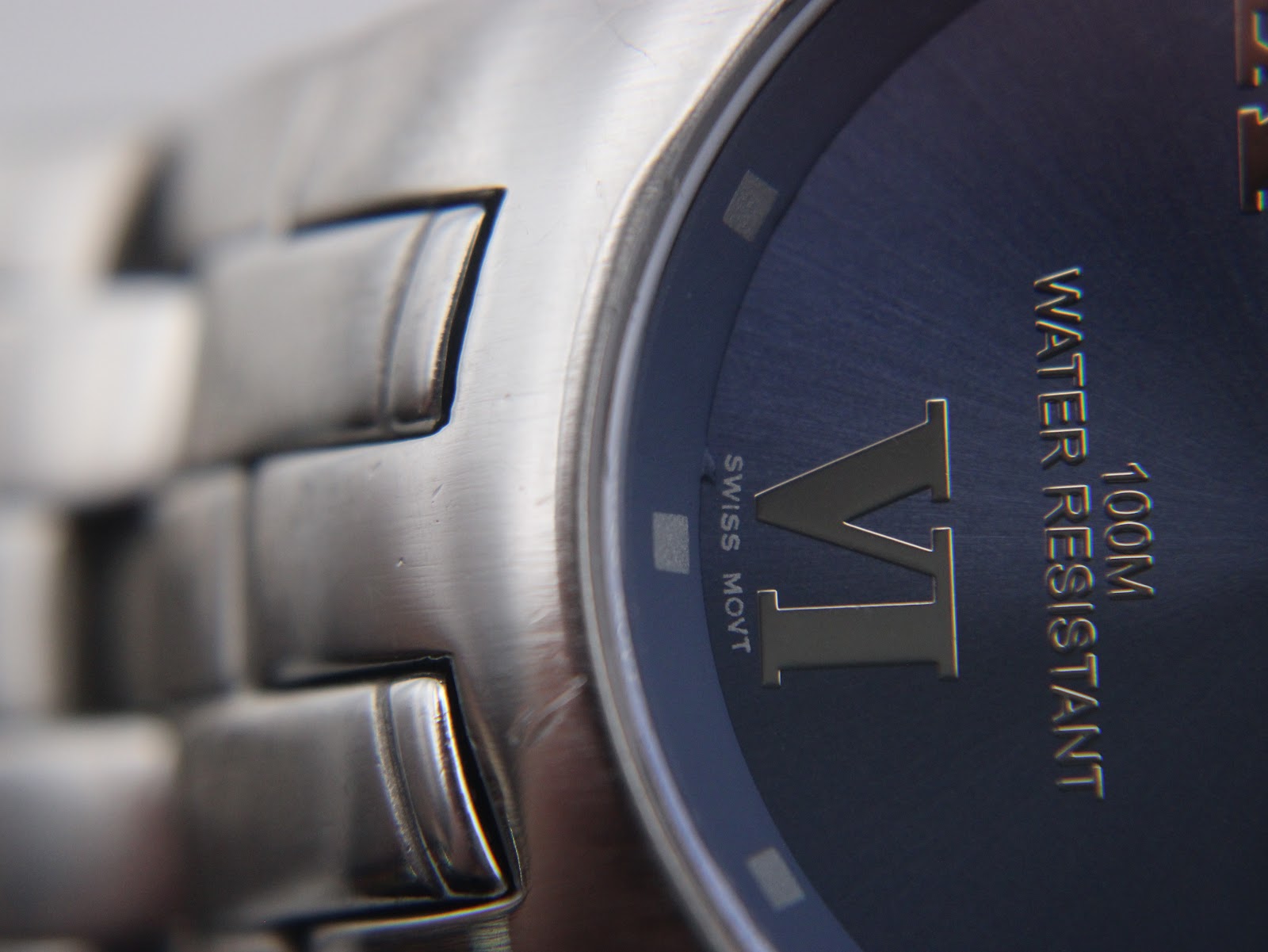 Macro shot of the watch dial edge and case, showing the 'VI' roman numeral, 'SWISS MOVT' text, and the watch's finish.