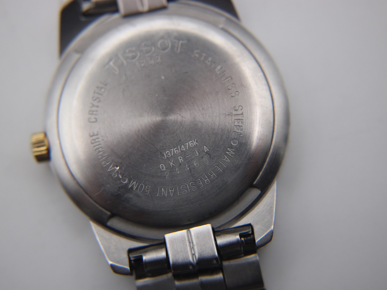 Close-up of the stainless steel case back of the Tissot PR 50, showing engravings like "Sapphire Crystal" and "50M Water Resistant".