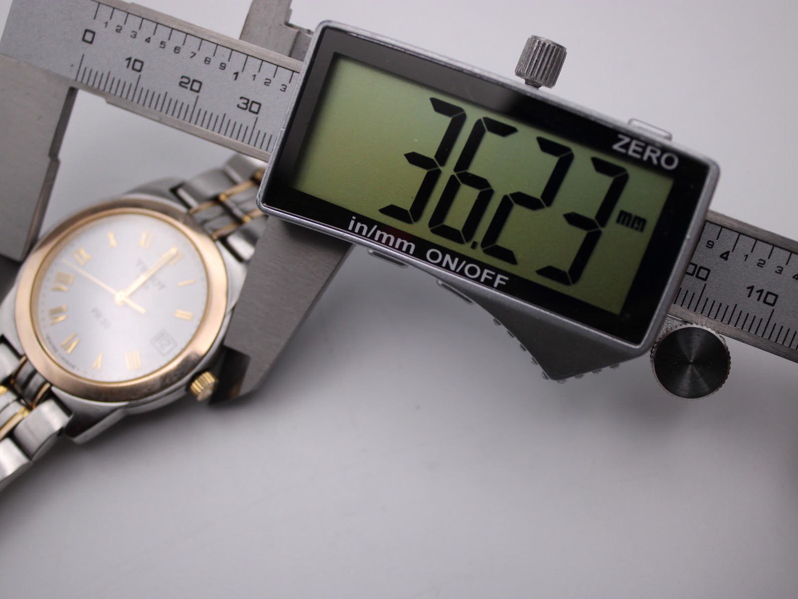 Digital caliper measuring the Tissot PR 50 case diameter at 36.23mm, with the watch visible in the background.