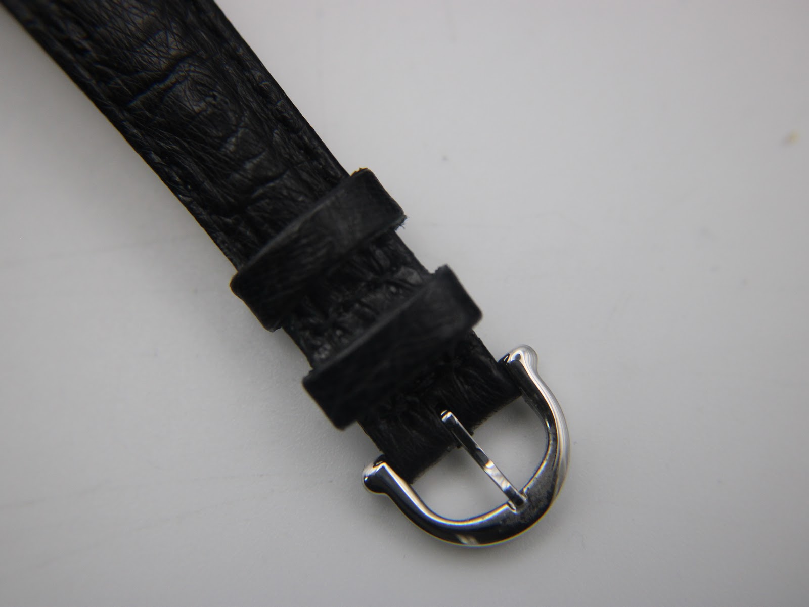 Close-up of the polished stainless steel pin buckle on the black leather strap.