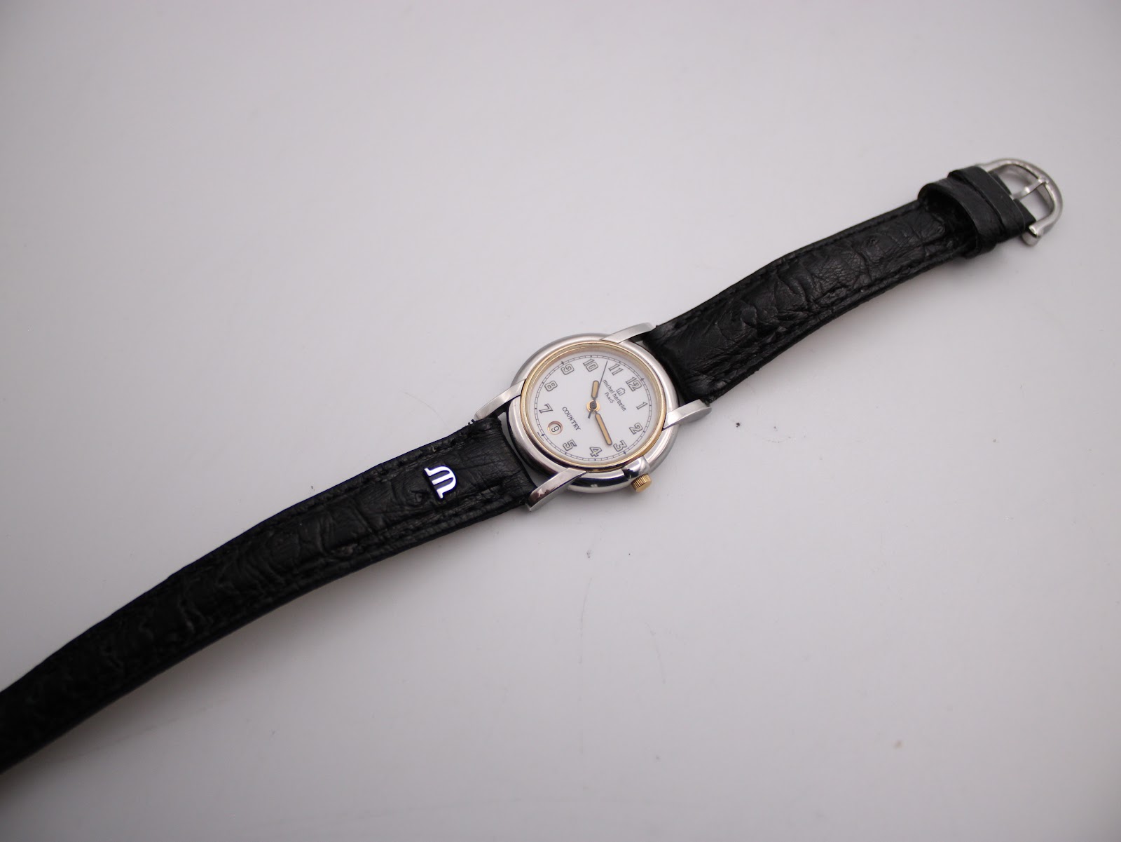 Full length view of the Michel Herbelin watch with its black leather strap laid flat.