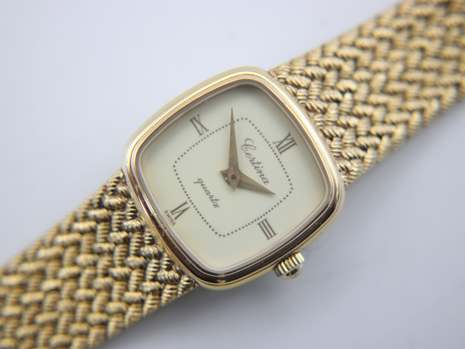 Top-down close-up of the champagne dial of the Certina watch, showing gold Roman numerals, dot minute track, and dauphine hands.